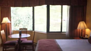 A hotel room with a bed, a table, two chairs, and a window with curtains.