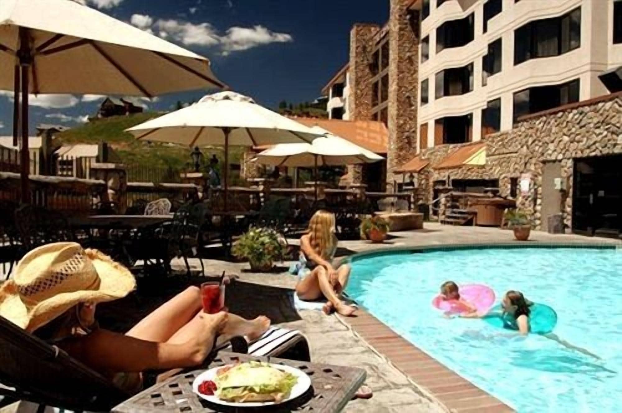 A poolside area with lounge chairs and umbrellas, a pool, and a building with multiple balconies.