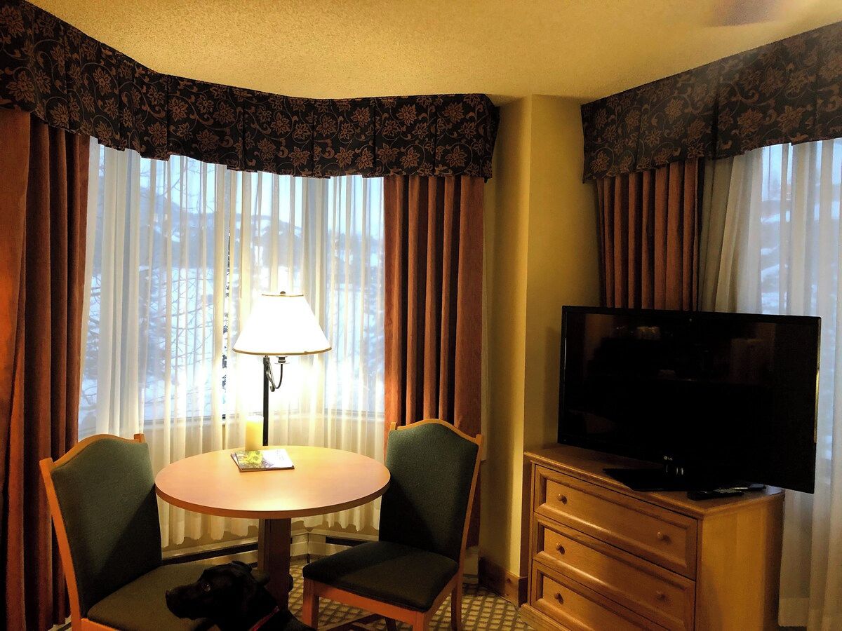 Een hotelkamer met een ronde tafel, twee stoelen, een televisie en een lamp.