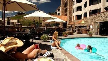 A poolside area with lounge chairs and umbrellas, a pool, and a building with multiple balconies.