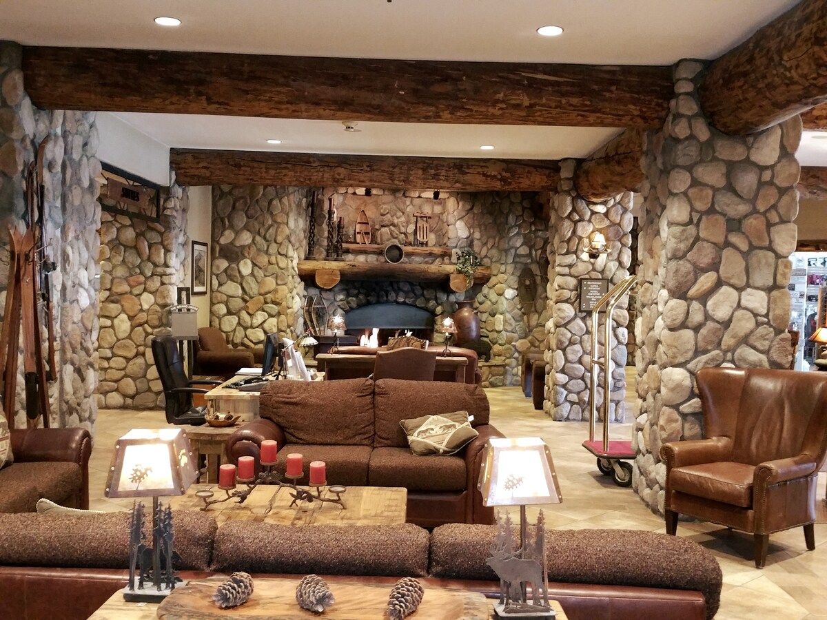 A cozy living room with a stone fireplace, leather furniture, and a rustic ceiling.