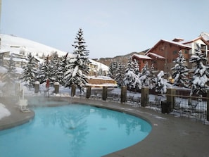 Une piscine entourée d’un paysage enneigé, avec des bâtiments en arrière-plan.