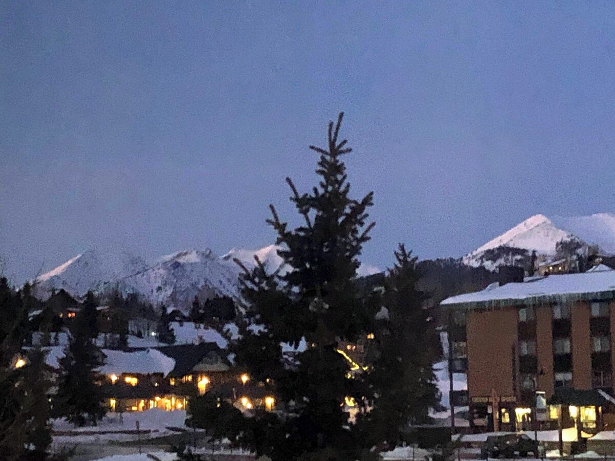 A hotel with a mountain backdrop, featuring a snow-covered peak and a building with illuminated windows.