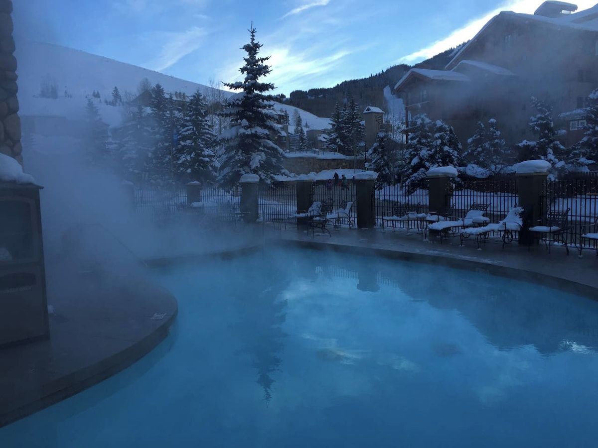 A snow-covered outdoor area with a pool, lounge chairs, and a mountainous backdrop.