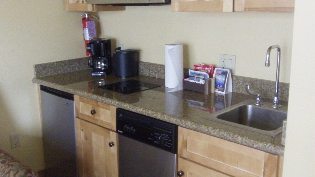 A compact kitchen with a dishwasher, a coffee maker, a paper towel dispenser, and a sink.