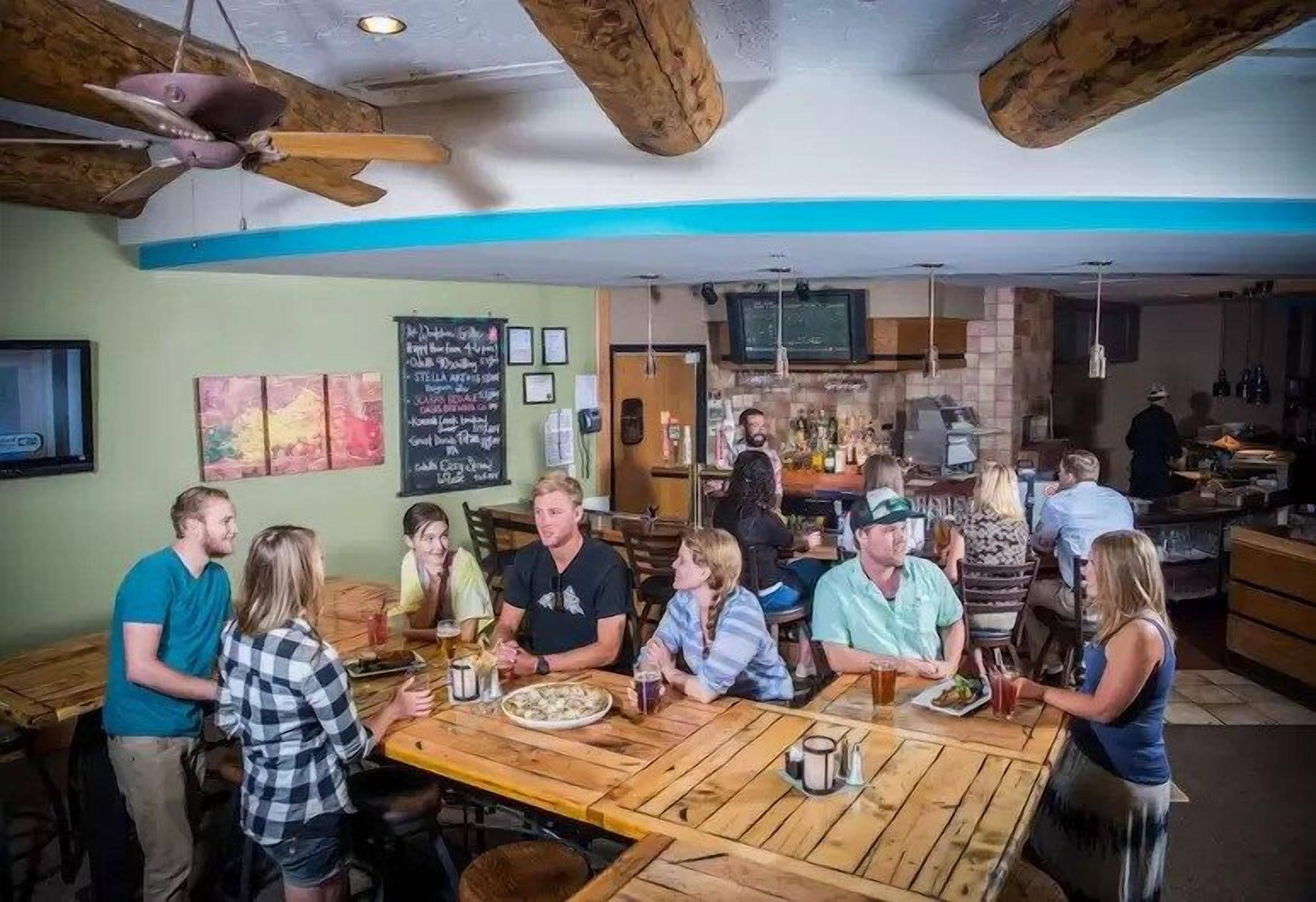 A group of people seated at a wooden table in a restaurant with a bar in the background.