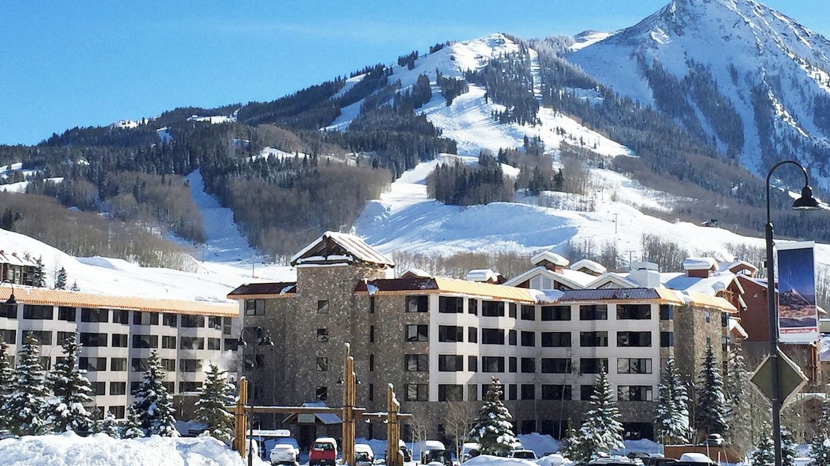Et hotel med flere etager, et skiområde i baggrunden og sneklædte omgivelser.