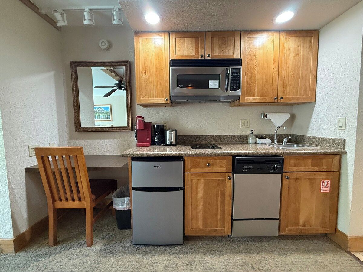 A compact kitchen with wooden cabinets, a microwave, a dishwasher, and a refrigerator.
