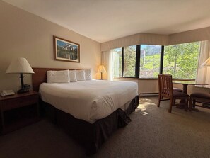 A hotel room with a large bed, a desk with a lamp, a chair, and a window with a view of greenery. - NEW LISTING - 223 Slopeside 2 King Beds @ Base (Crested Butte)