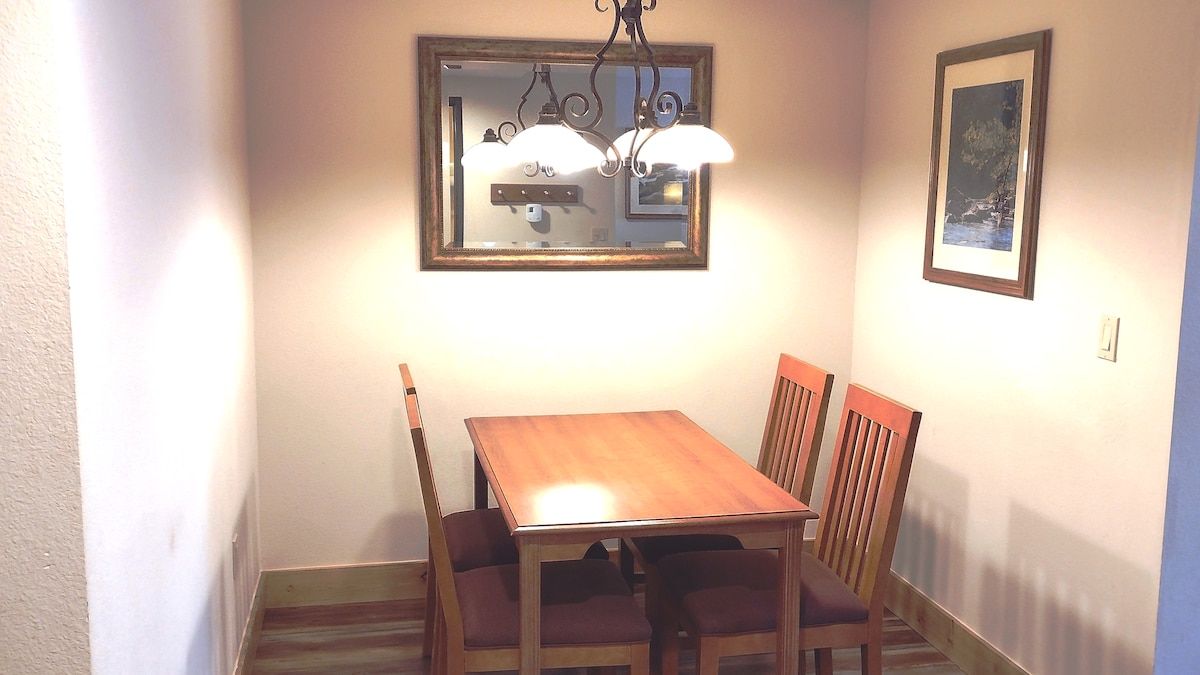 A dining area with a wooden table and chairs, a chandelier, a mirror, and a framed picture on the wall.