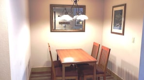 Un coin repas avec une table et des chaises en bois, un lustre, un miroir et un tableau encadré accroché au mur.
