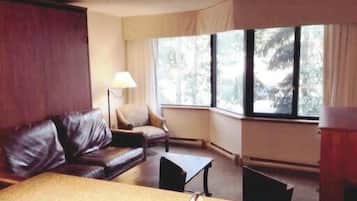 A room with a leather sofa, a small table, and a lamp. There are windows with curtains.
