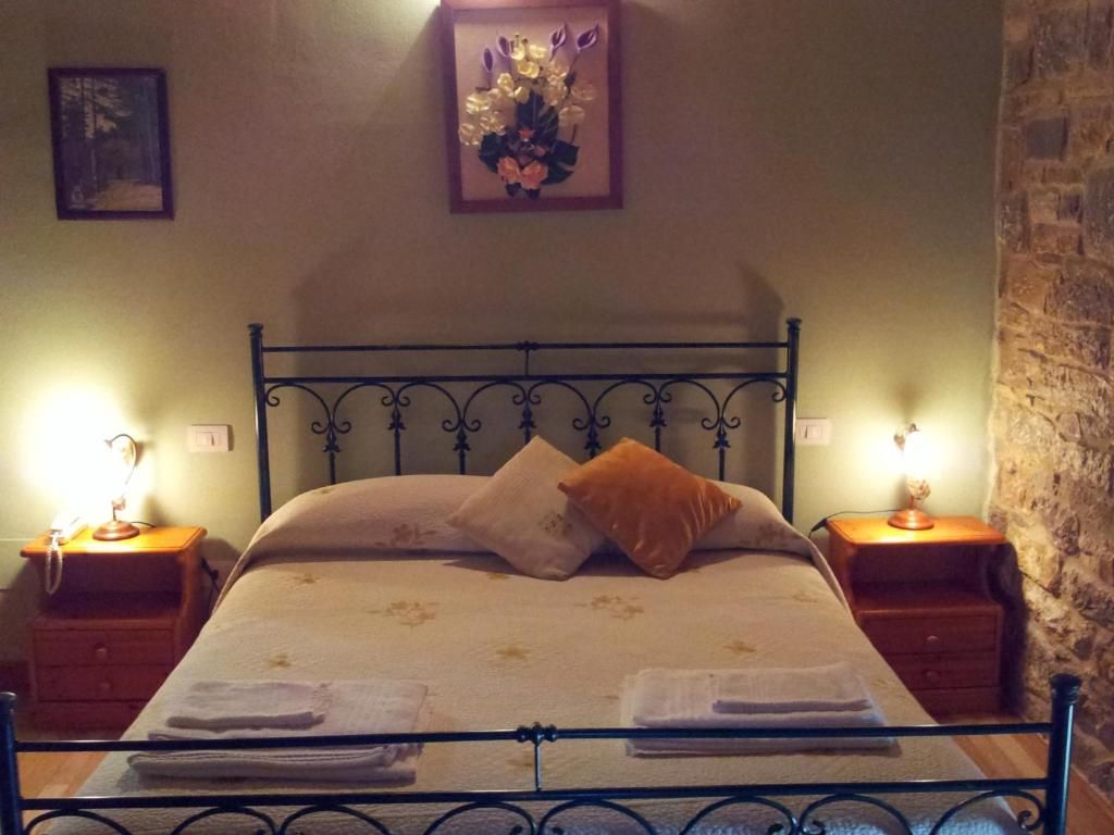 Un letto con struttura in metallo, due comodini, un mobiletto e un quadro appeso al muro, con una parete in pietra.