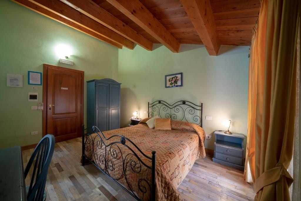 Un dormitori amb sostre de fusta, un llit amb estructura metàl·lica, una tauleta de nit, un armari i una porta.
