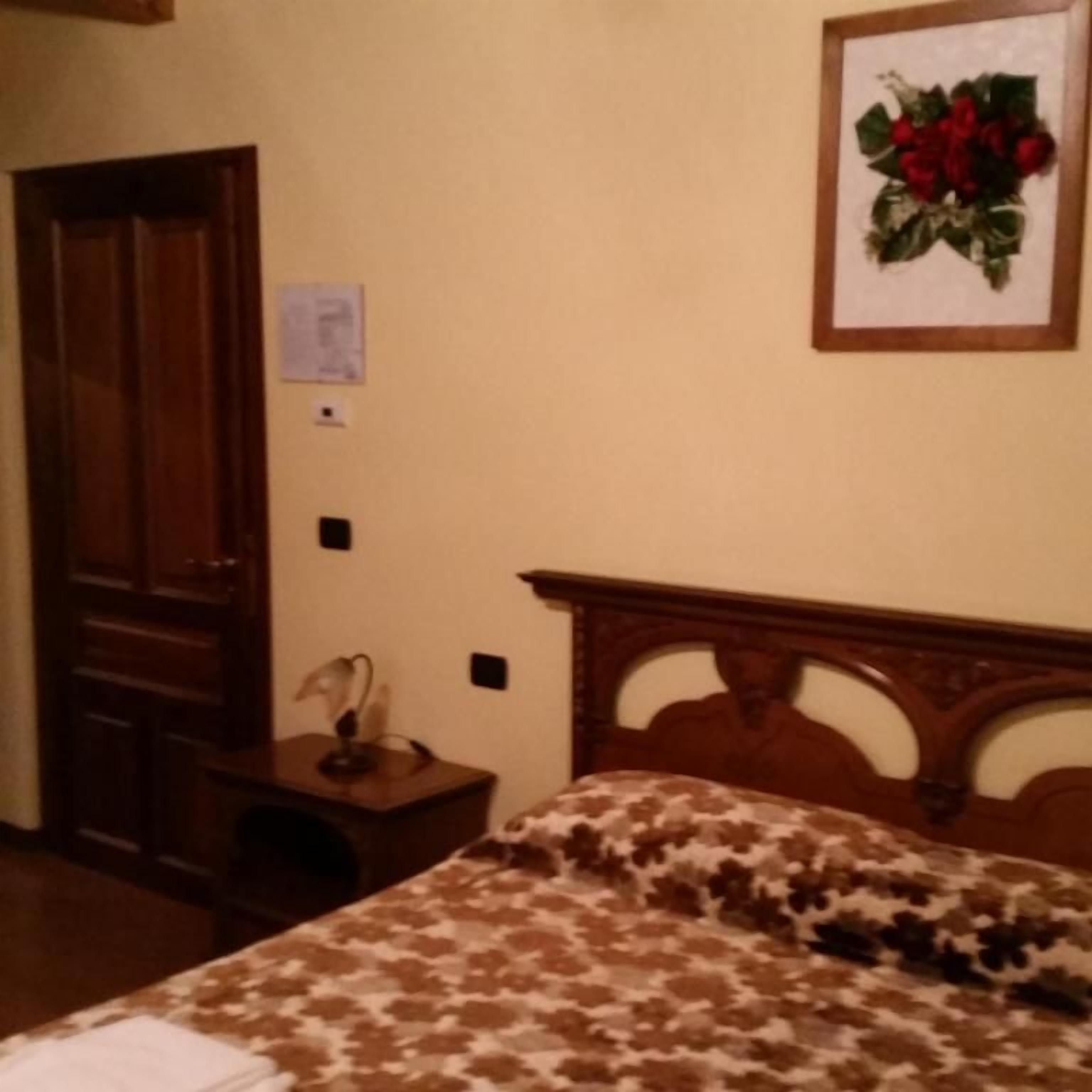 Un dormitorio con cabecera de madera, cama con cubrecama estampado, mesita de noche con lámpara y un cuadro enmarcado en la pared.