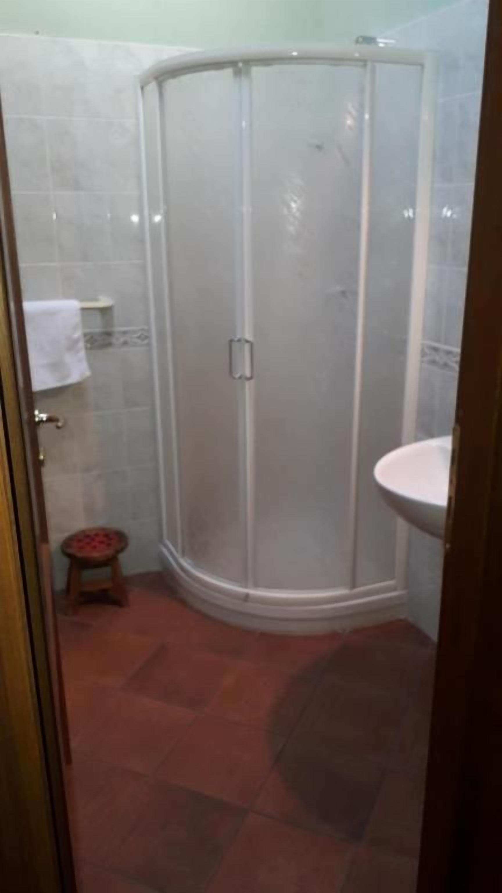 Un baño con ducha envuelta en vidrio, un lavamanos y un taburete pequeño.