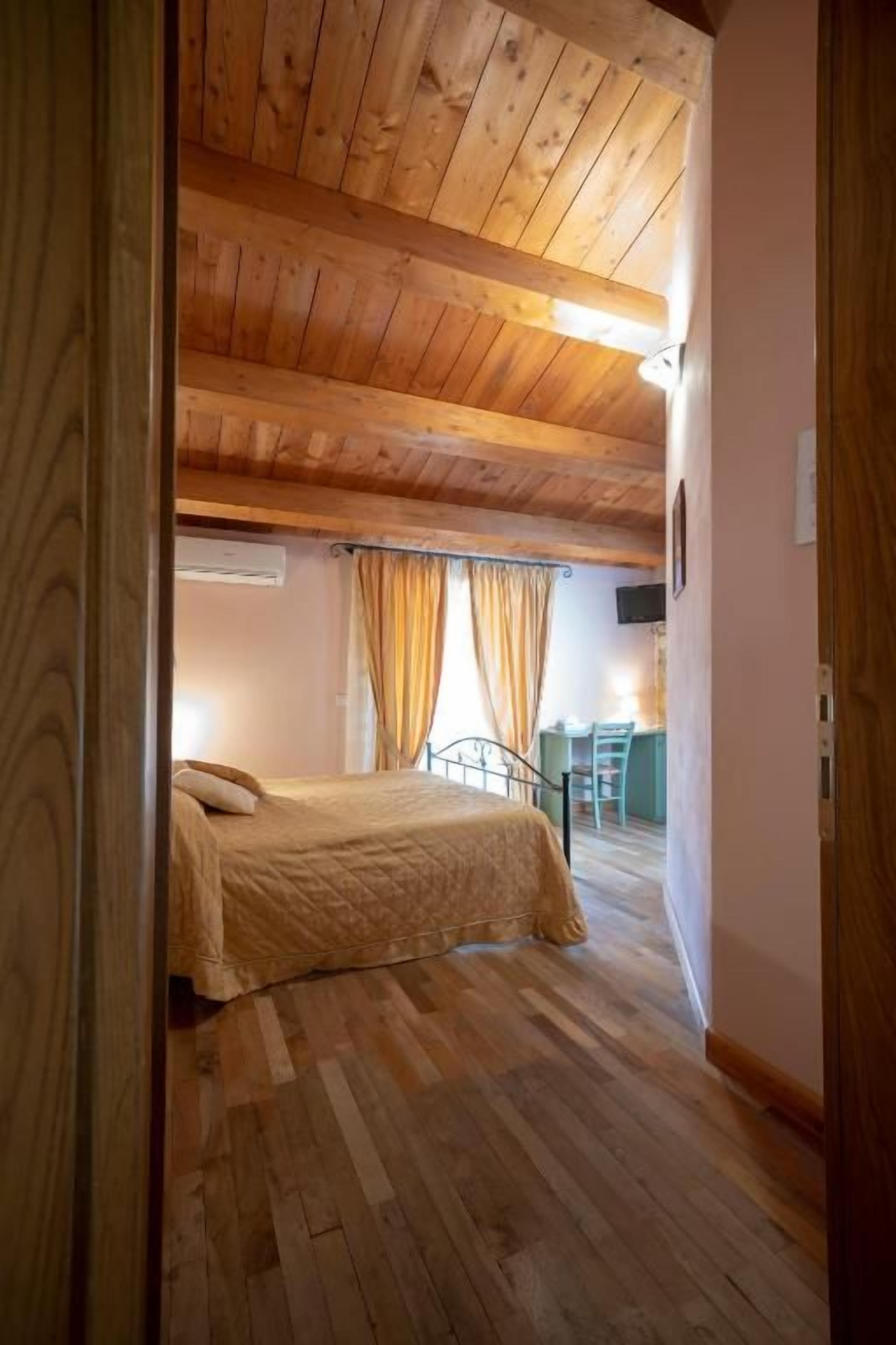 A bedroom with a wooden ceiling, a bed, a desk, and curtains.