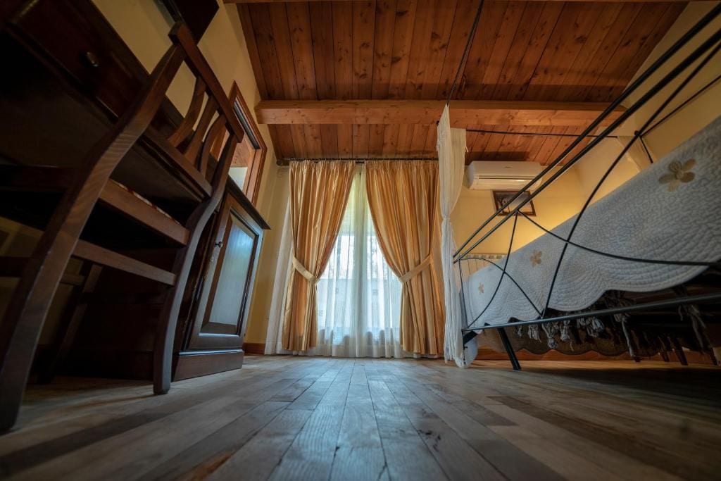 Una habitación con piso de madera, una cama con cubrecama blanco y una ventana con cortinas.