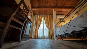 Una habitación con piso de madera, una cama con cubrecama blanco y una ventana con cortinas.