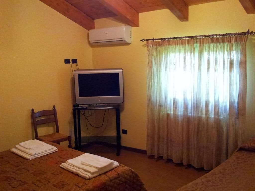 A room with a bed, a chair, a television on a stand, and a window with curtains.