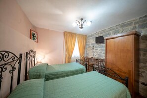 Una habitación con dos camas, una pared de piedra, un armario de madera y un televisor montado en la pared.