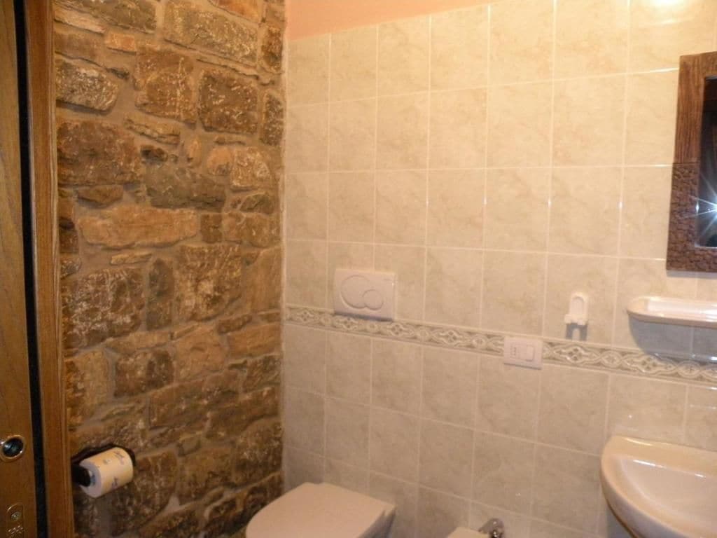 Un baño con pared de piedra, inodoro, lavabo y espejo.
