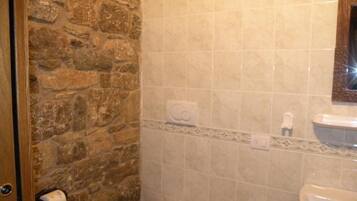 Un baño con pared de piedra, inodoro, lavabo y espejo.