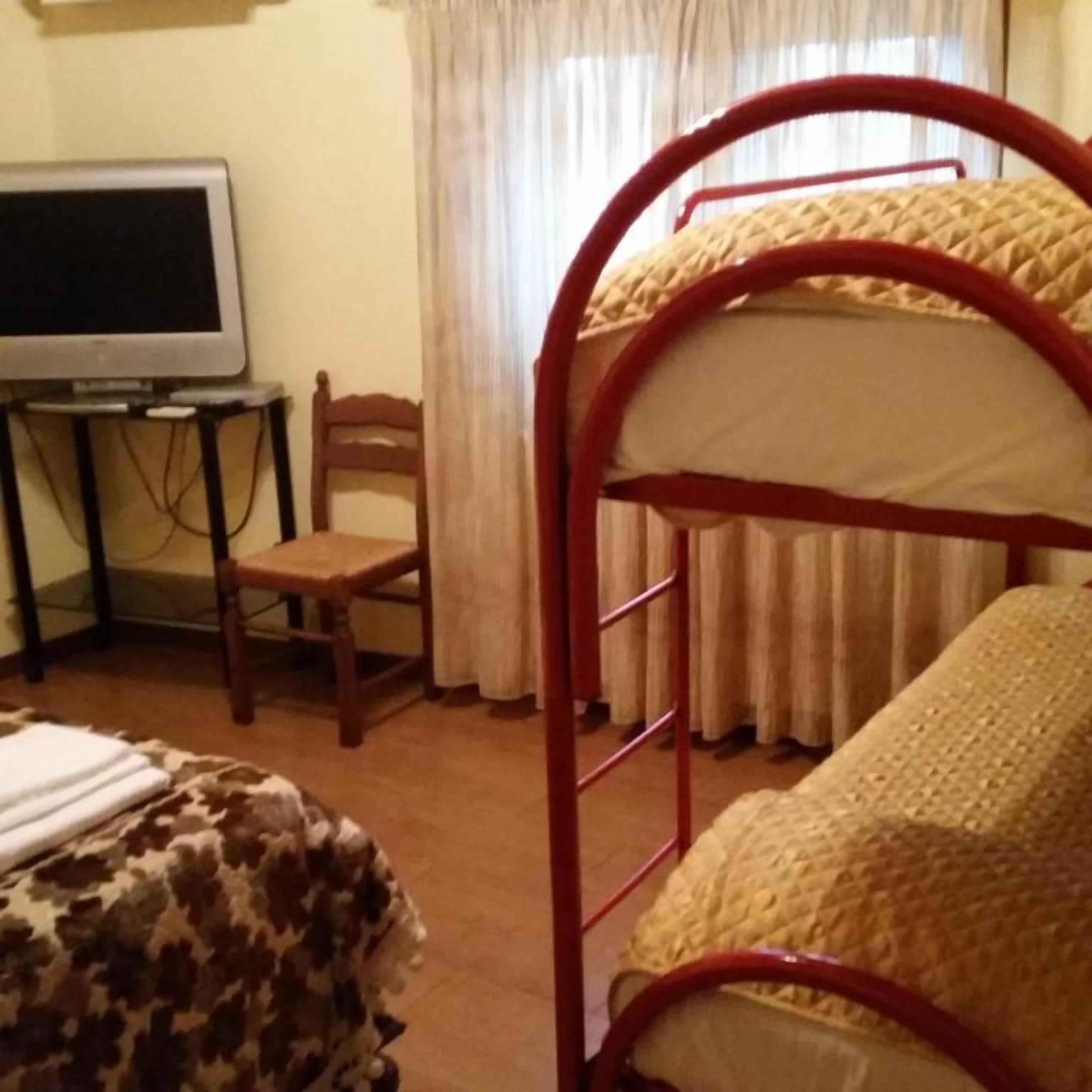 Una habitación con una cama litera, un televisor sobre un mueble, una silla y una ventana con cortinas.