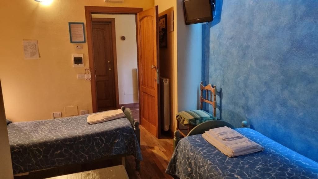 A room with two beds, a wooden door, a wall-mounted TV, and a blue wall.