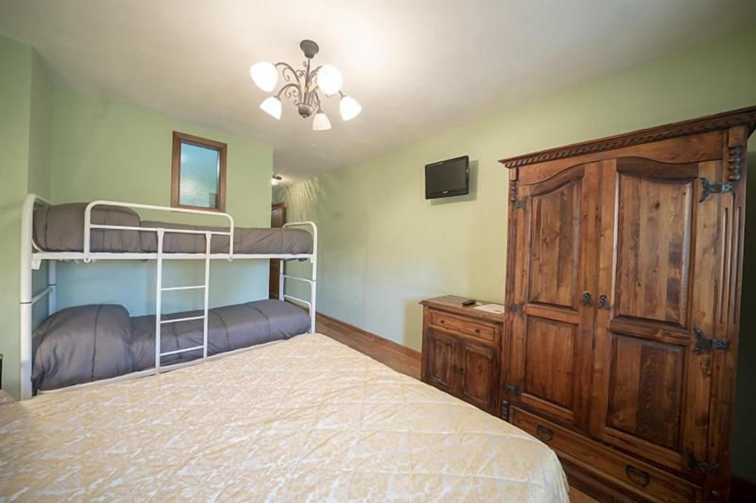 Ein Zimmer mit Etagenbetten, einem Holzschrank und einem an der Wand befestigten Fernseher.
