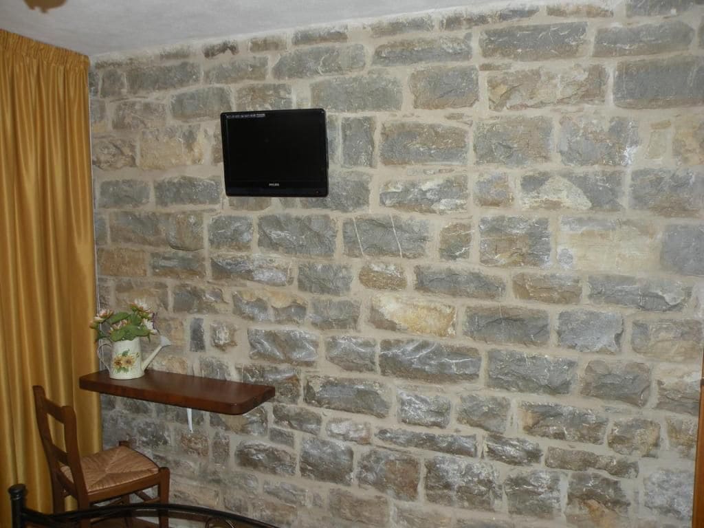 Una pared de piedra con un televisor de pantalla plana montado sobre un estante de madera.