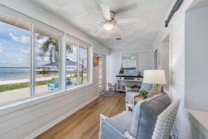 Amplia habitación con grandes ventanales con vista a la playa, un ventilador de techo y una zona de estar acogedora con una lámpara.