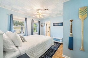Une chambre avec un lit, un ventilateur de plafond, une fenêtre avec des rideaux, un éventail mural et un panneau indiquant « endroit où l’on est bien ».