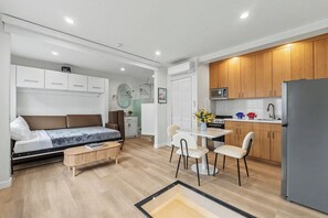 Un espace de vie compact comprenant un lit, un petit coin repas, une kitchenette et une salle de bain.