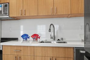 A kitchen with wooden cabinets, a stainless steel sink, and two decorative fish-shaped containers. - The Coastal Nest Beachside Getaway steps to Pier (Santa Monica)