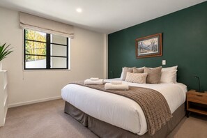 Ein Schlafzimmer mit einem großen Bett, einem Fenster mit Jalousien, einem Bild an der Wand und einem Nachttisch.