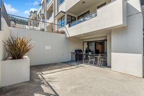 Un edificio moderno con techo plano, balcón con barandas de metal y un pequeño espacio al aire libre con sillas y una mesa.