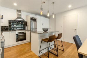 Una cocina moderna con electrodomésticos de acero inoxidable, una isla central con taburetes e iluminación colgante.