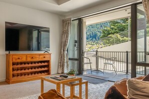 A living room with a flat-screen TV, wooden wine rack, and a balcony with metal chairs. - Central Courtyard - Free parking · 250 m to town (Queenstown)