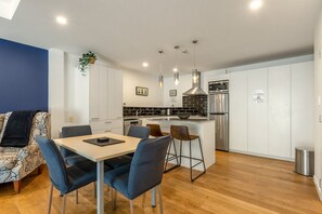 Una cocina moderna con armarios blancos, un refrigerador de acero inoxidable y una zona de comedor con mesa y sillas.