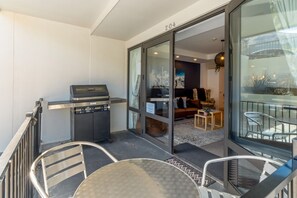 Ein Balkon mit Grill, eine Sitzecke mit Sofa und Stühlen und Blick in ein Wohnzimmer.