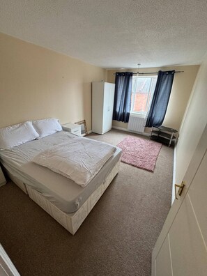 A bedroom with a bed, a wardrobe, a window with curtains, and a carpeted floor. - Charming 1-bedroom Apartment in West Northamptonshire (Northampton)