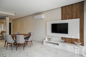 A modern dining area with a round table and chairs, a mounted flat-screen TV, and a white console with drawers. - Lakeview Residence Serviced By BlueKeys (New Cairo)