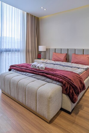 A modern hotel room with a large bed, a bedside table with a lamp, and a view of the outdoors through sheer curtains. - Lakeview Residence Serviced By BlueKeys (New Cairo)