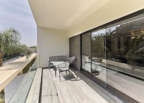 Un área de estar exterior moderna con una partición de vidrio, una terraza de madera y vistas a la calle y al verde.
