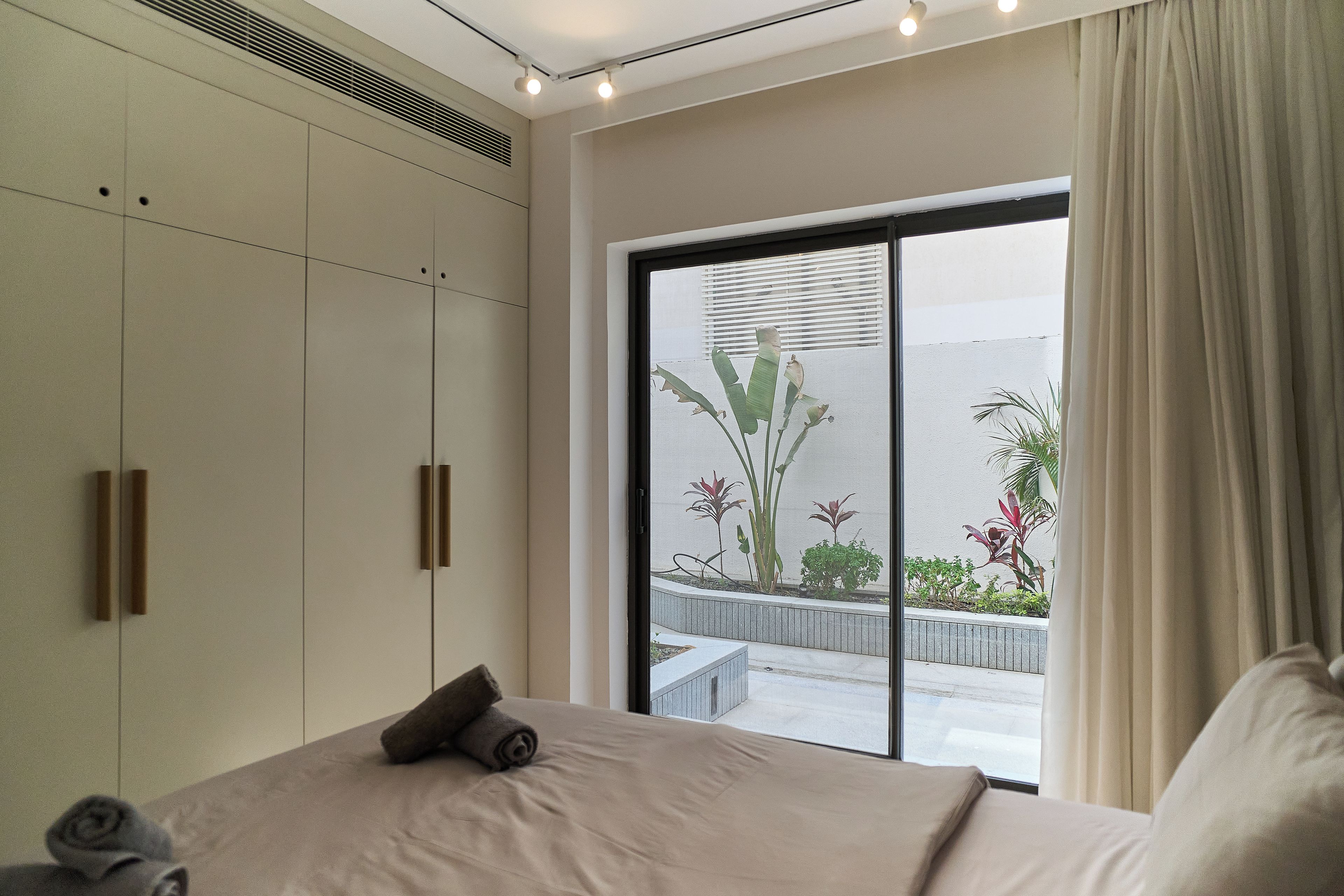 A bedroom with a large bed, a wardrobe, and a view of a balcony with plants.