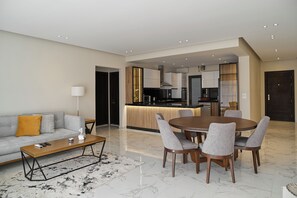 A modern living room with a sofa, coffee table, and dining area with chairs. - Lakeview Residence Serviced By BlueKeys (New Cairo)