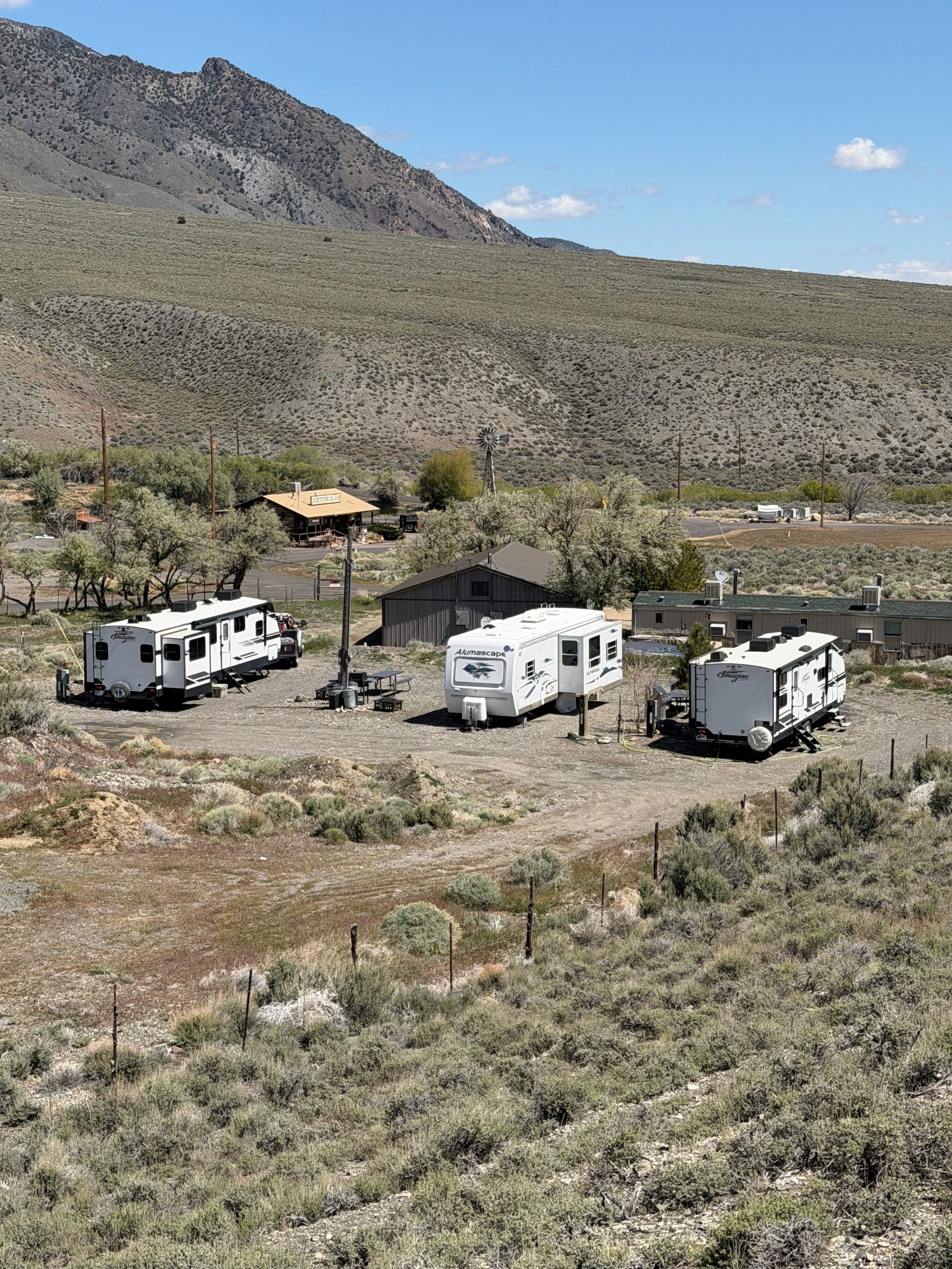 A campsite with RVs and a small building, surrounded by sparse vegetation and a mountain in the background.