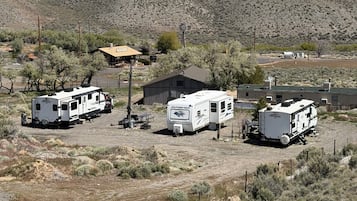 A campsite with RVs and a small building, surrounded by sparse vegetation and a mountain in the background.