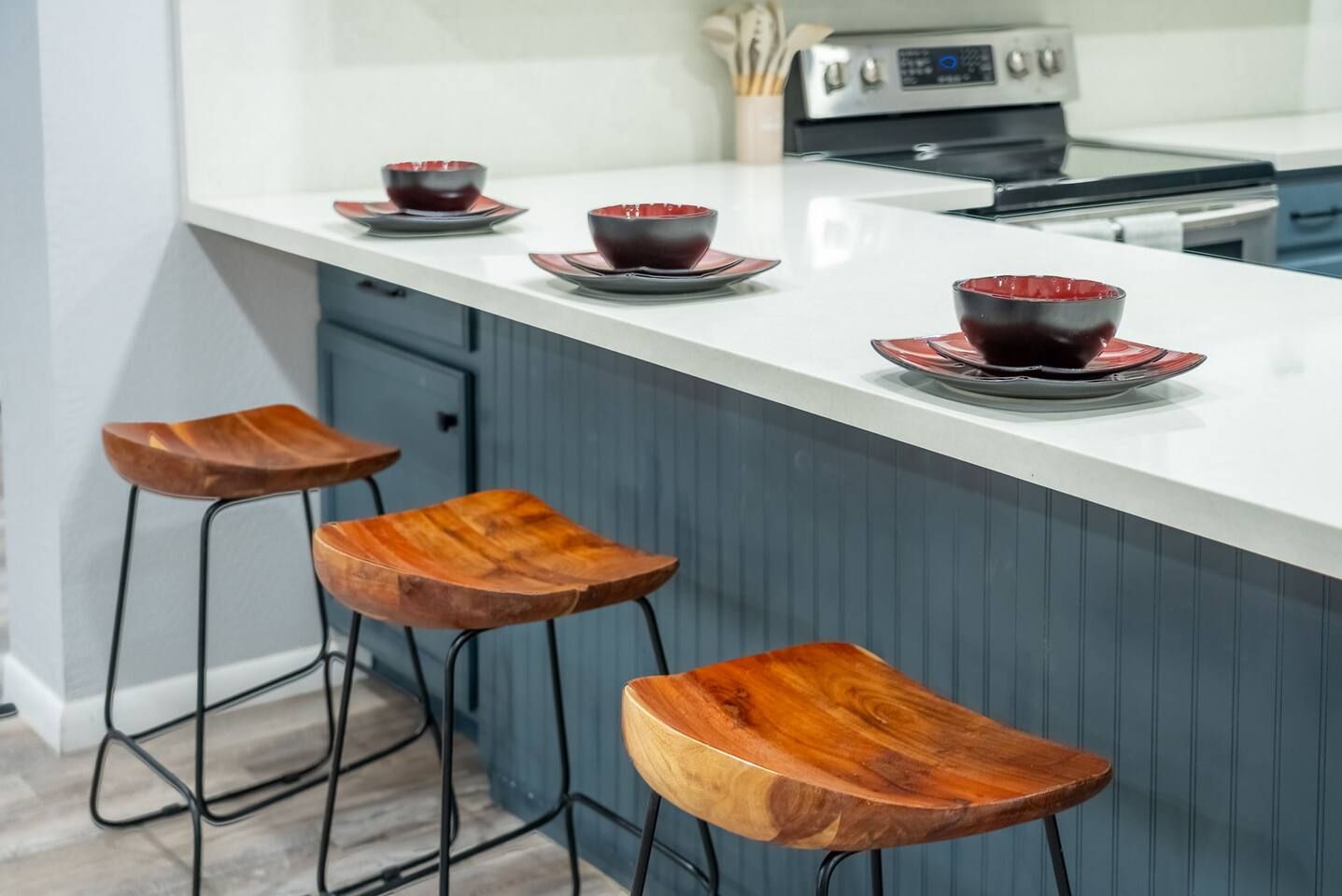 A kitchen island with a white countertop, three wooden stools, and a set of red and black bowls on the counter.